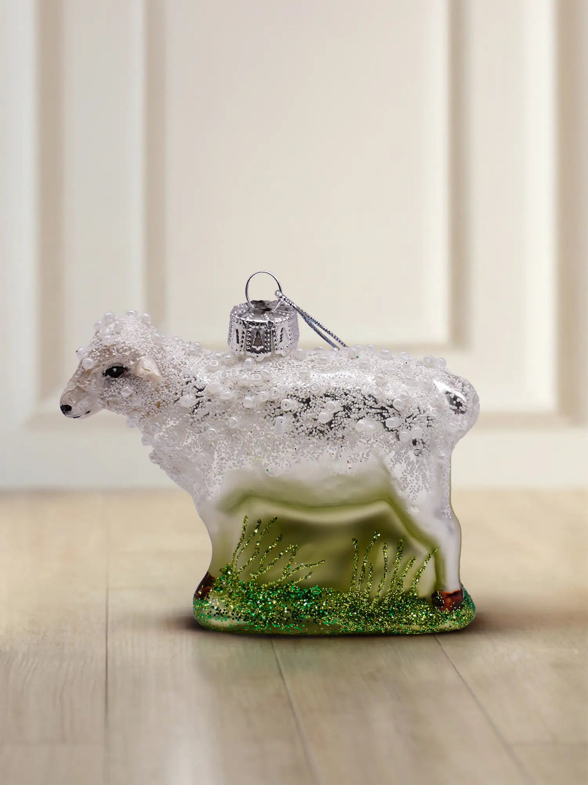 Glasornament Schaf: weißes Glasschaf auf grüner Wiese, Fell mit weißen Perlendetails und feinem Glitzer, silberner Aufhänger mit silberner Kordel