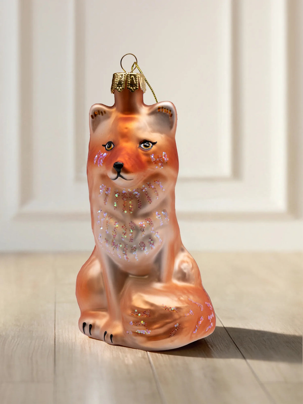 Glasornament Fuchs: sitzender Fuchs in Orange und Creme mit schillernden Glitzerakzenten an Wangen, Brust und Schwanz, goldene Aufhängekappe