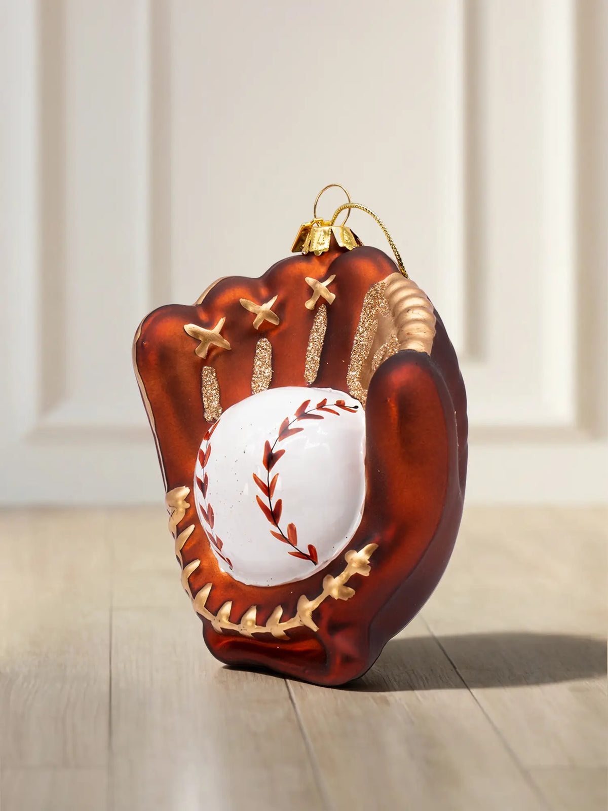 Glasornament in Form eines braunen Baseballhandschuhs mit goldenen Nähten und weißem Baseball mit roten Stichen.