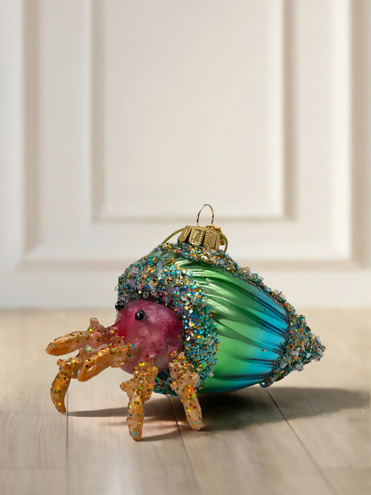 Glasornament Krabbe in Muschel: Pinke Krabbe mit orangefarbenen Beinen und Glitzer, grün-türkises Schneckenhaus mit buntem Glitzerbesatz am Rand, goldene Aufhängekappe