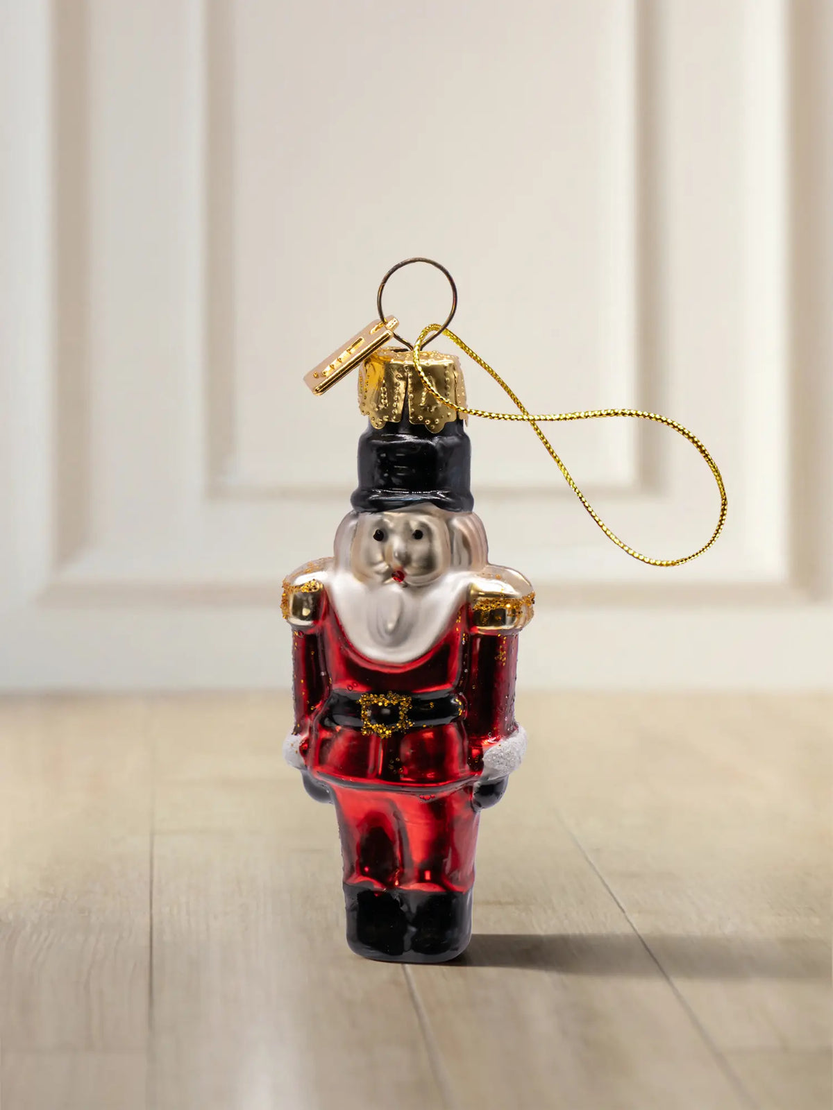 Glasornament Nussknacker klein: roter Nussknacker mit schwarzem Hut, weißem Bart und goldenen Schulterabzeichen, goldenes Hängeelement