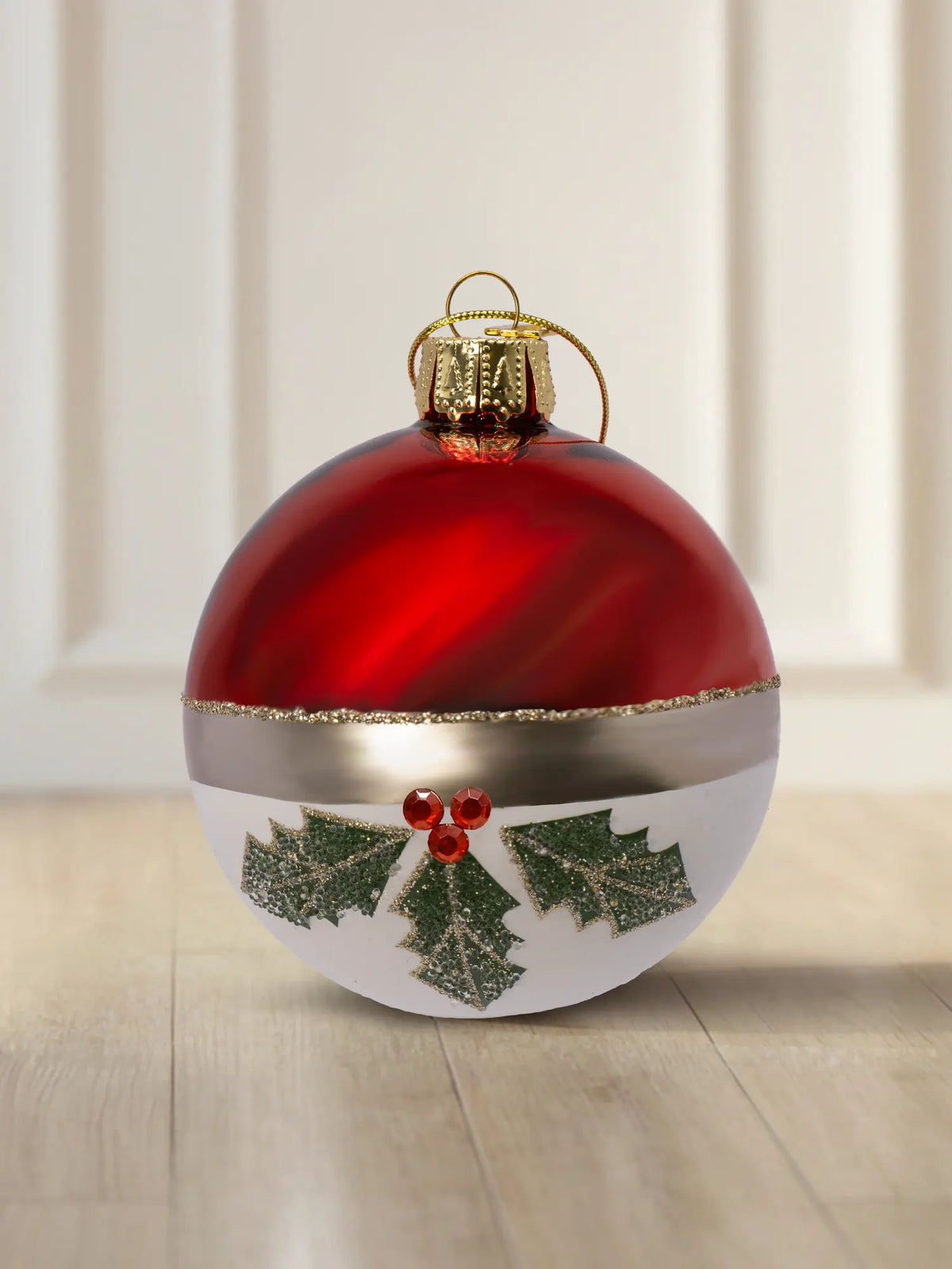 Glaskugel Winterbeerenzweig 10cm: obere Hälfte rot glänzend, untere Hälfte weiß matt, goldener Glitzerstreifen als Trennlinie, grüne Stechpalmenzweige mit roten Straßsteinen, goldener Aufhänger mit goldener Kordel
