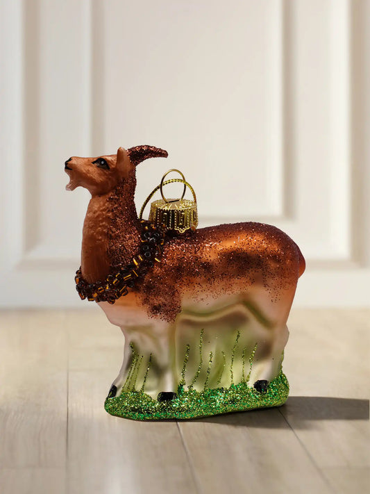 Glasornament Ziegenbock: brauner Bock mit Glitzerfell, Perlenkette um den Hals und grünem Glitzergras am Sockel, goldene Aufhängekappe