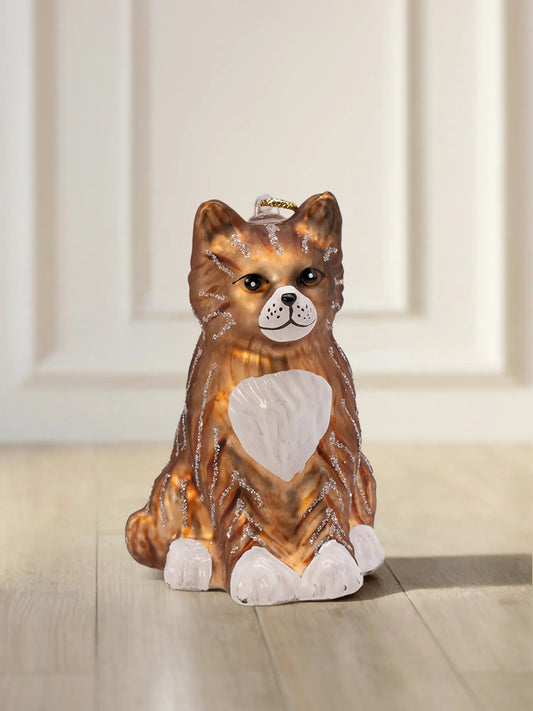 Glasornament in Form einer sitzenden getigerten Katze mit orangebraunem Fell, silbernen Glitzerstreifen, weißer Brust und weißen Pfoten.