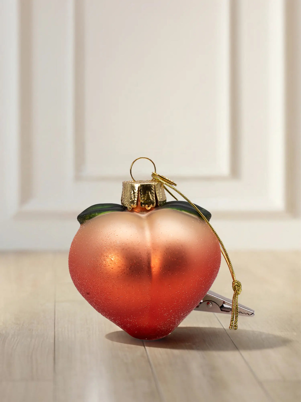 Mattes Glasornament in Form eines Pfirsichs mit Farbverlauf von Pfirsich zu Orangerot, grünen Blättern, goldener Kappe und Klammer.