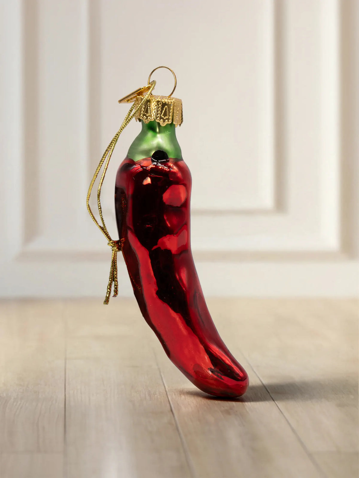 Glasornament in Form einer roten Chilischote mit grünem Stielansatz, goldener Kappe und Goldkordel.