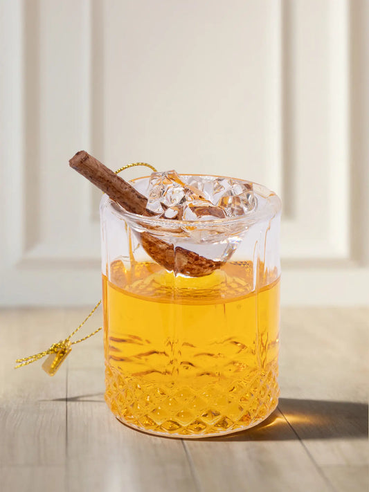 Gläsernes Ornament in Form eines Whiskyglases mit Kristallschliff, goldgelber Flüssigkeit, Eiswürfeln und einer Zimtstange.