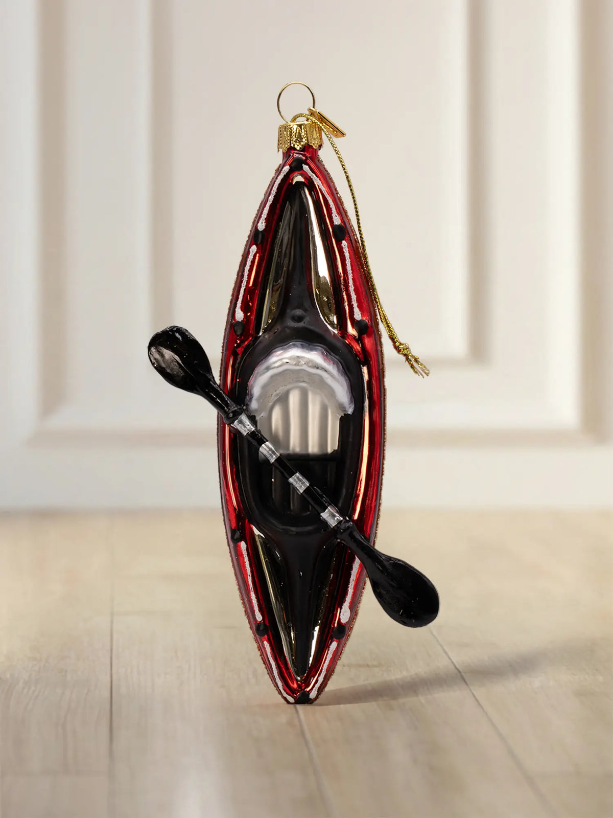 Glasornament in Form eines roten Kajaks in Draufsicht mit schwarzem Paddel und goldener Aufhängung.