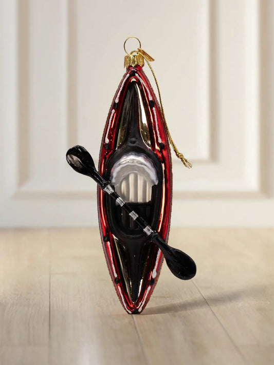 Glasornament in Form eines roten Kajaks in Draufsicht mit schwarzem Paddel und goldener Aufhängung.