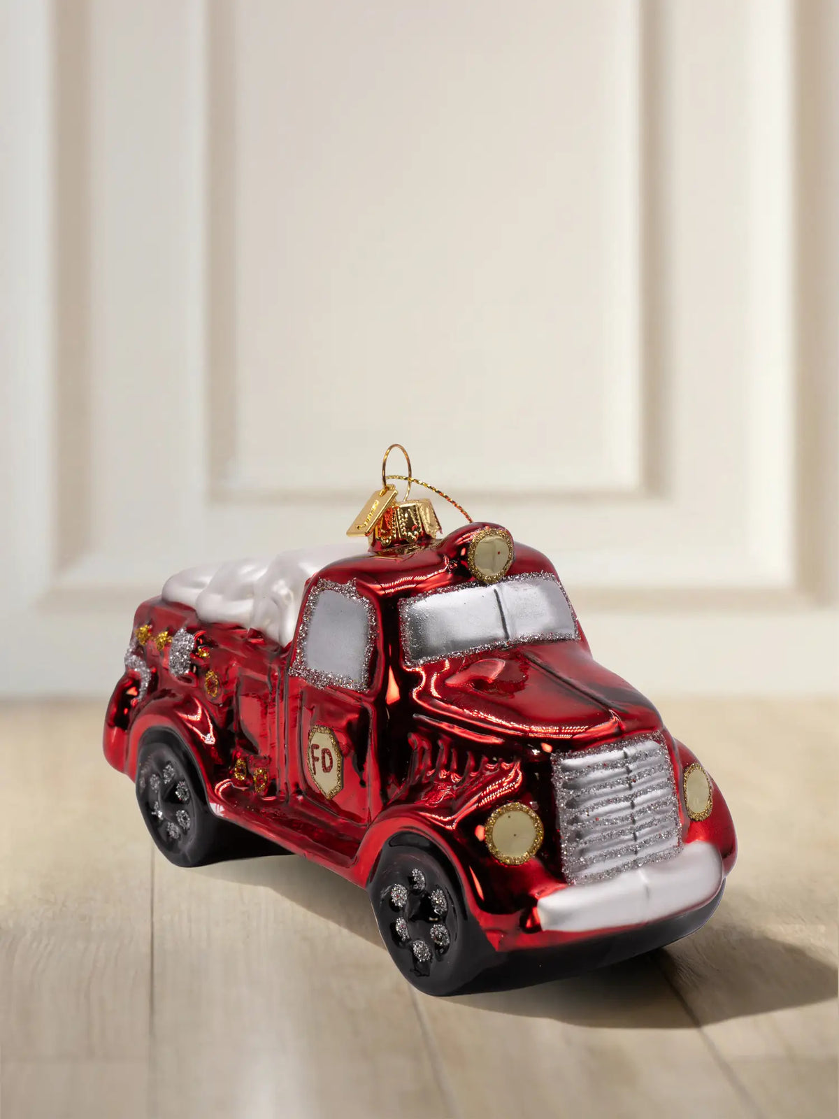 Glasornament Feuerwehrauto: rotes glänzendes Löschfahrzeug mit „FD”-Emblem, silbernem Kühlergrill, Glitzerakzenten und goldener Aufhängekappe