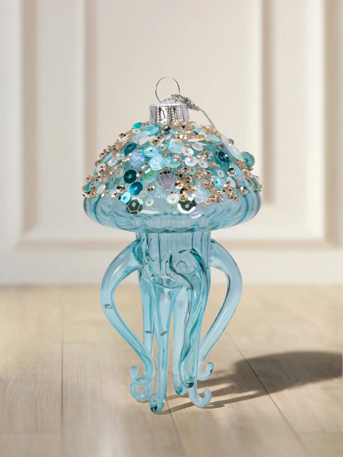 Gläsernes Ornament in Form einer türkisblauen Qualle mit Pailletten und Muschelmotiven auf dem Schirm, Silberkappe und vier geschwungenen Tentakeln.