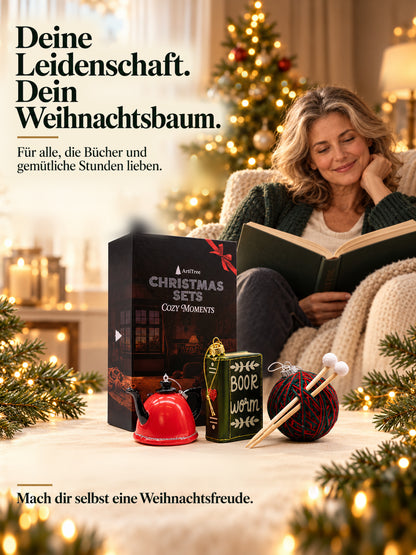 ArtiTree Glasfigurenset Cozy Moments – Lifestyle-Aufnahme mit Person und Tagline „Für alle, die Gemütlichkeit lieben", Box und alle drei Glasfiguren, goldene Weihnachtslichter im Hintergrund