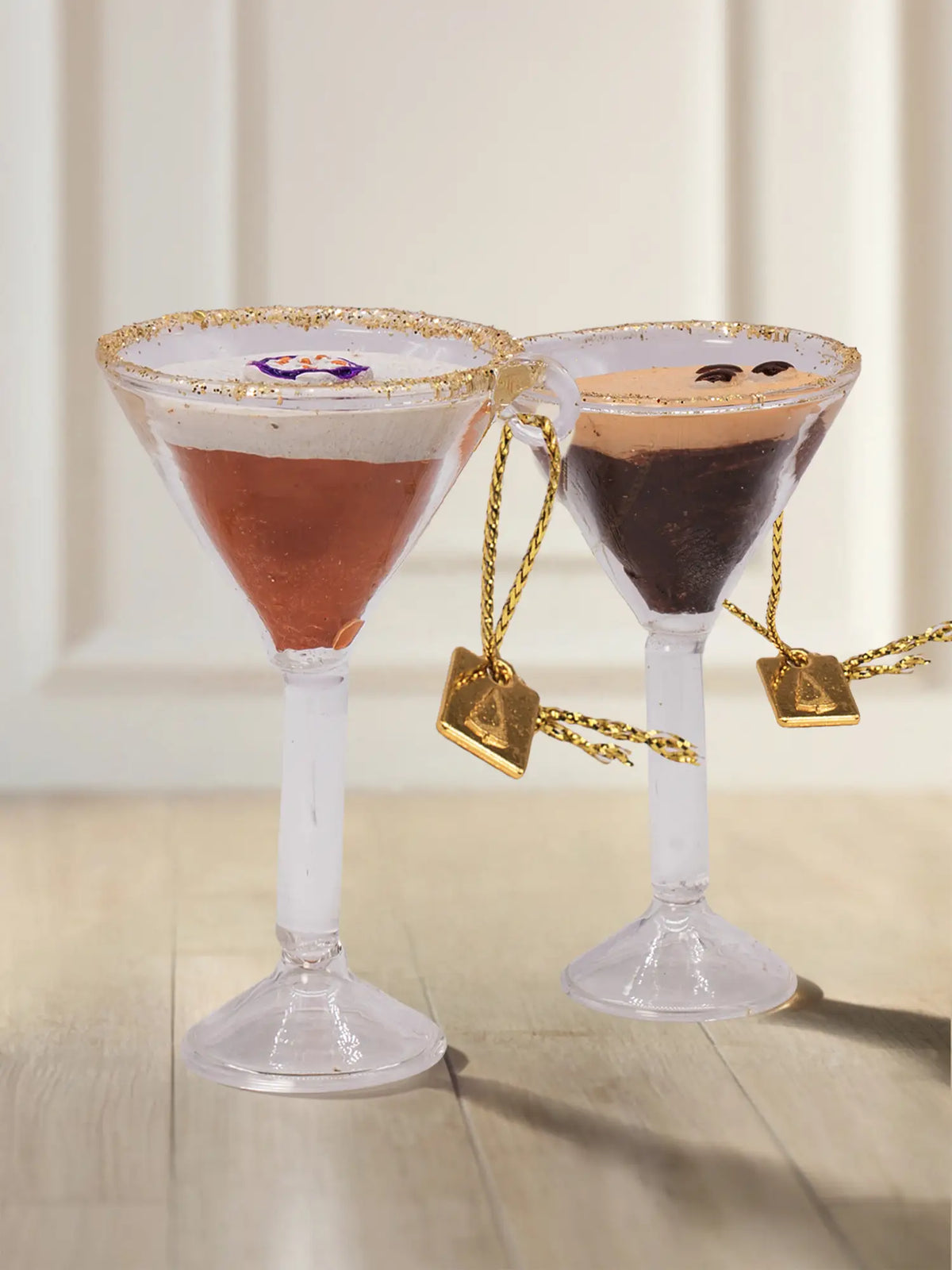 Glasornament Cocktailgläser: zwei Coupette-Gläser mit Espresso Martini (dunkelbraun mit Glitzercrema und drei Kaffeebohnen) und orangefarbenem Passionsfrucht-Cocktail mit weißem Schaum und Fruchthälfte, mit goldenen Kordeln