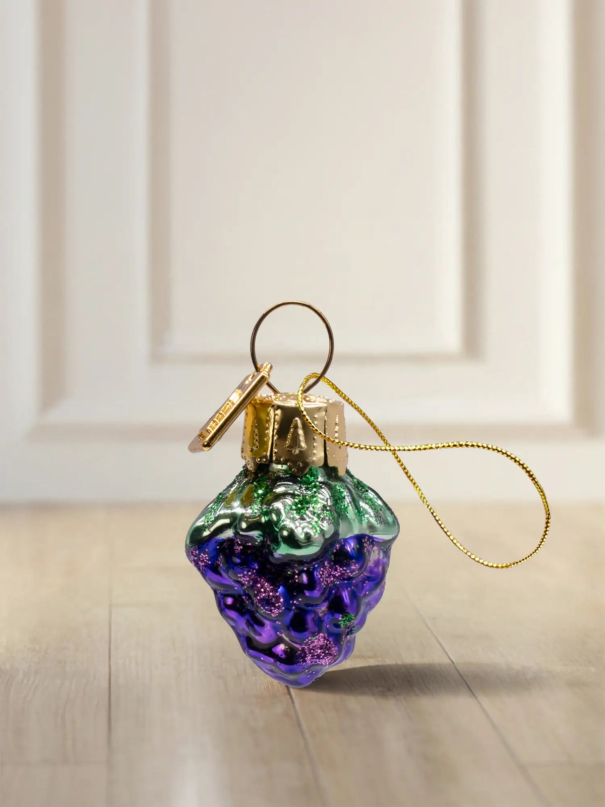 Glasornament Traube: kleine, blau-violette Weintraube mit grünem Stiel und lila Glitter-Finish, goldenes Hängeelement