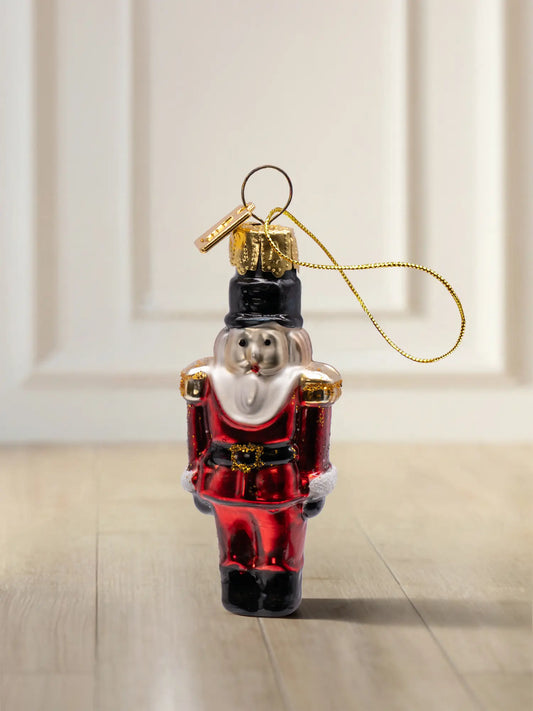 Glasornament Nussknacker klein: roter Nussknacker mit schwarzem Hut, weißem Bart und goldenen Schulterabzeichen, goldenes Hängeelement