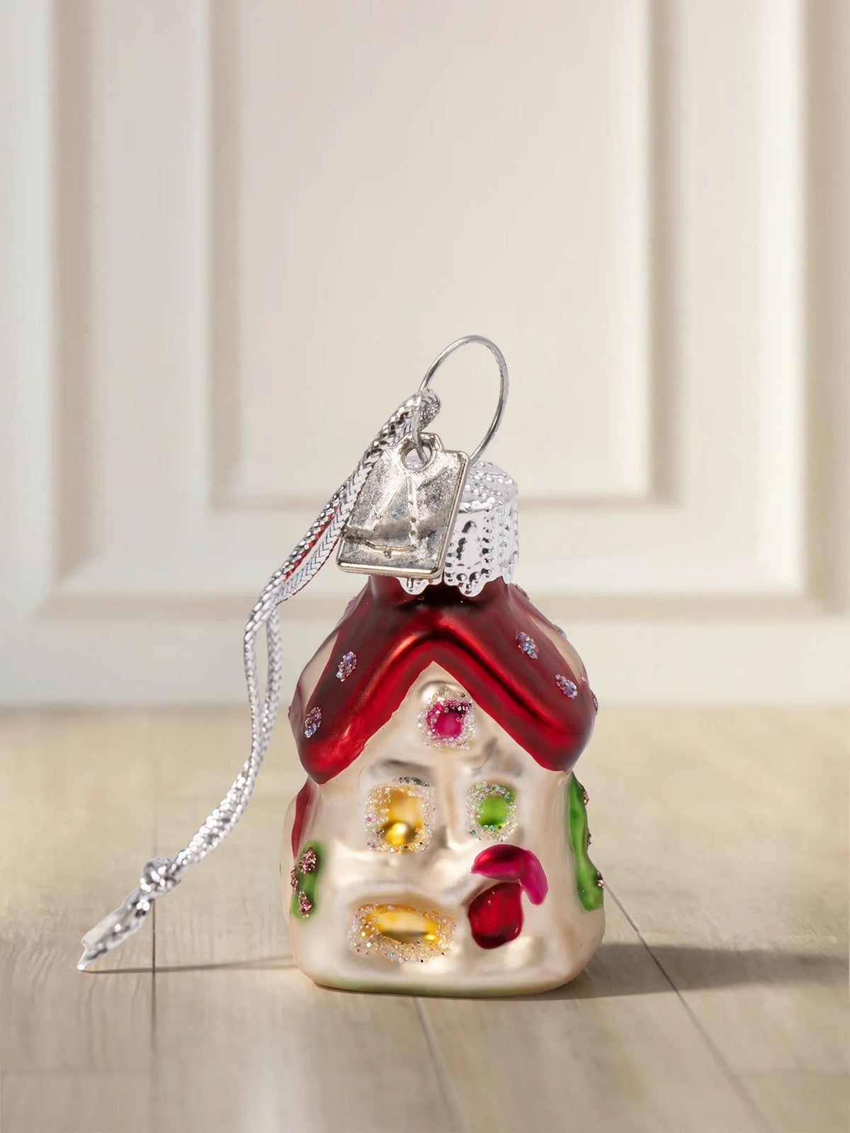 Glasornament Haus: weiß-cremefarbenes Lebkuchenhaus mit rotem Dach, bunter Zuckerdekoration in Rosa, Grün und Gelb, silbernes Hängeelement