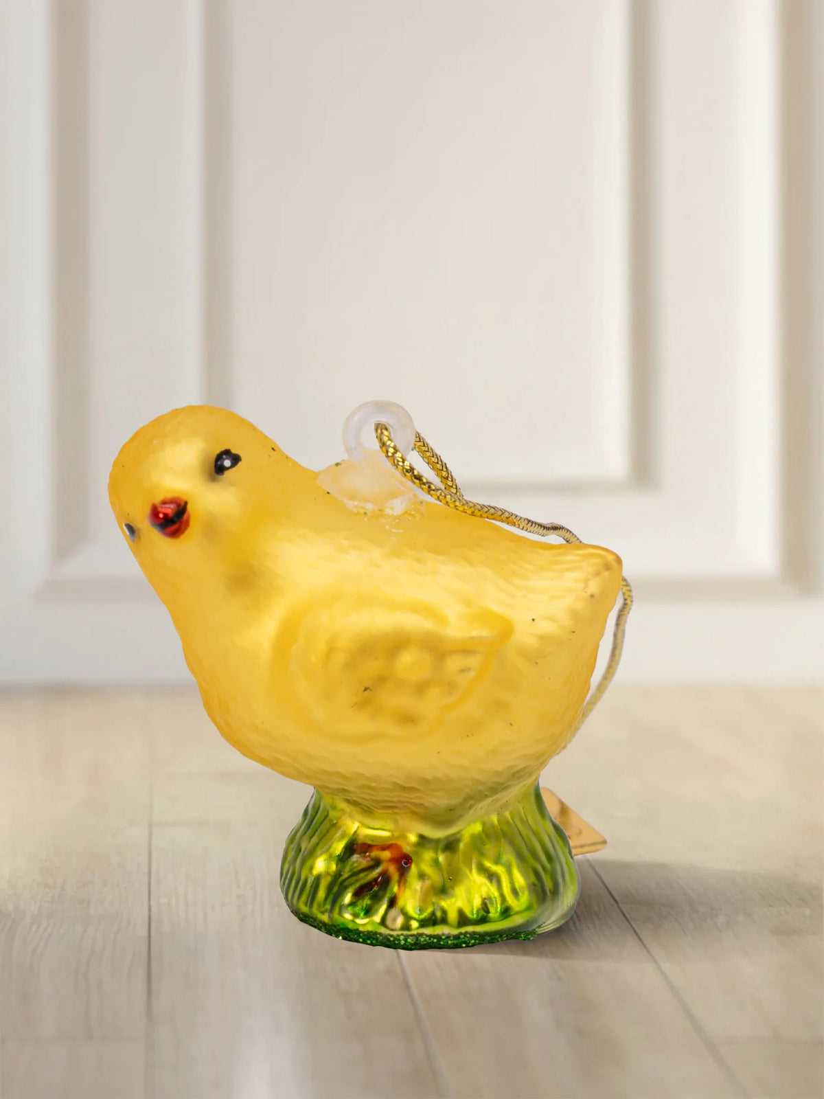 Glasornament Küken: gelbes Küken auf grünem Grassockel, matt-gelbes Finish mit roten Wangen, goldenes Hängeelement