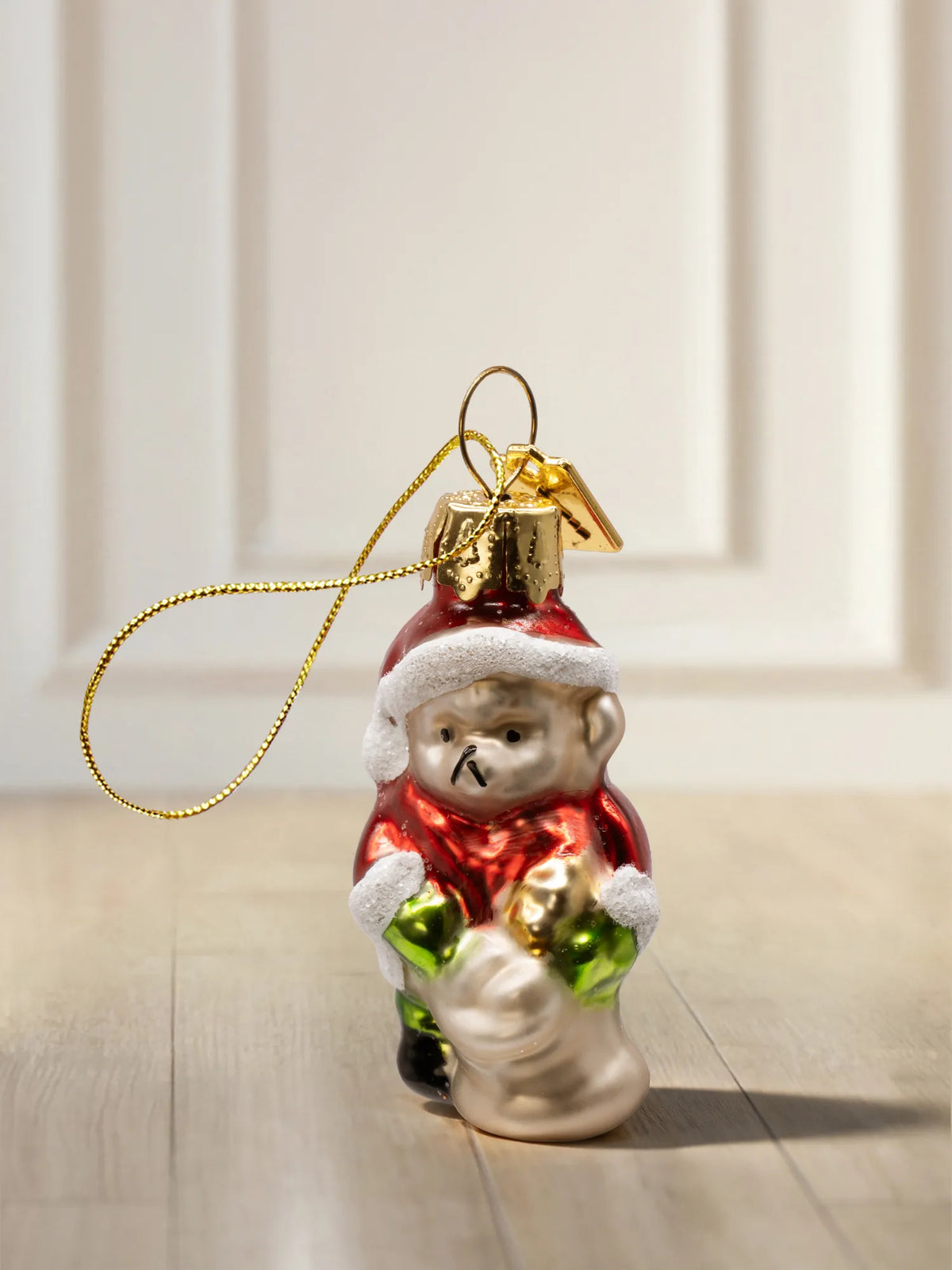Glasornament Weihnachtsteddy: brauner Teddybär im roten Weihnachtsmantel mit weißer Mütze, hält goldenes Geschenk, goldenes Hängeelement