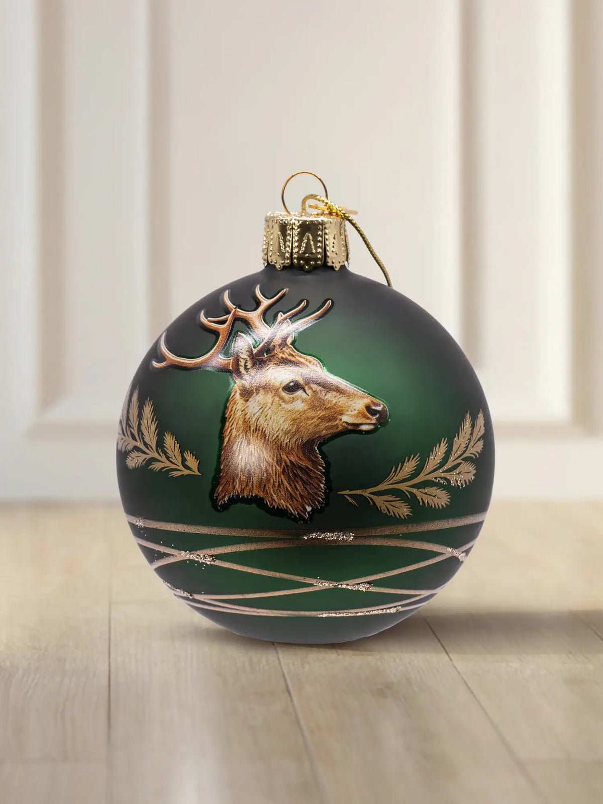 Glaskugel grün matt mit Hirsch 10cm: dunkelgrüne matte Glaskugel, aufgesetztes Hirschkopf-Motiv mit Geweih, goldene Farnblatt-Details und goldene Schraffurlinien, goldener Aufhänger mit goldener Kordel