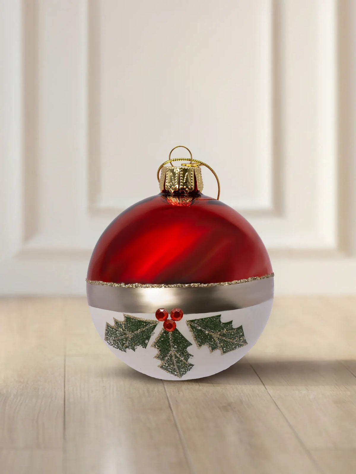 Glaskugel Winterbeerenzweig 6cm: obere Hälfte rot glänzend, untere Hälfte weiß matt, goldener Glitzerstreifen als Trennlinie, grüne Stechpalmenzweige mit roten Straßsteinen, goldener Aufhänger mit goldener Kordel