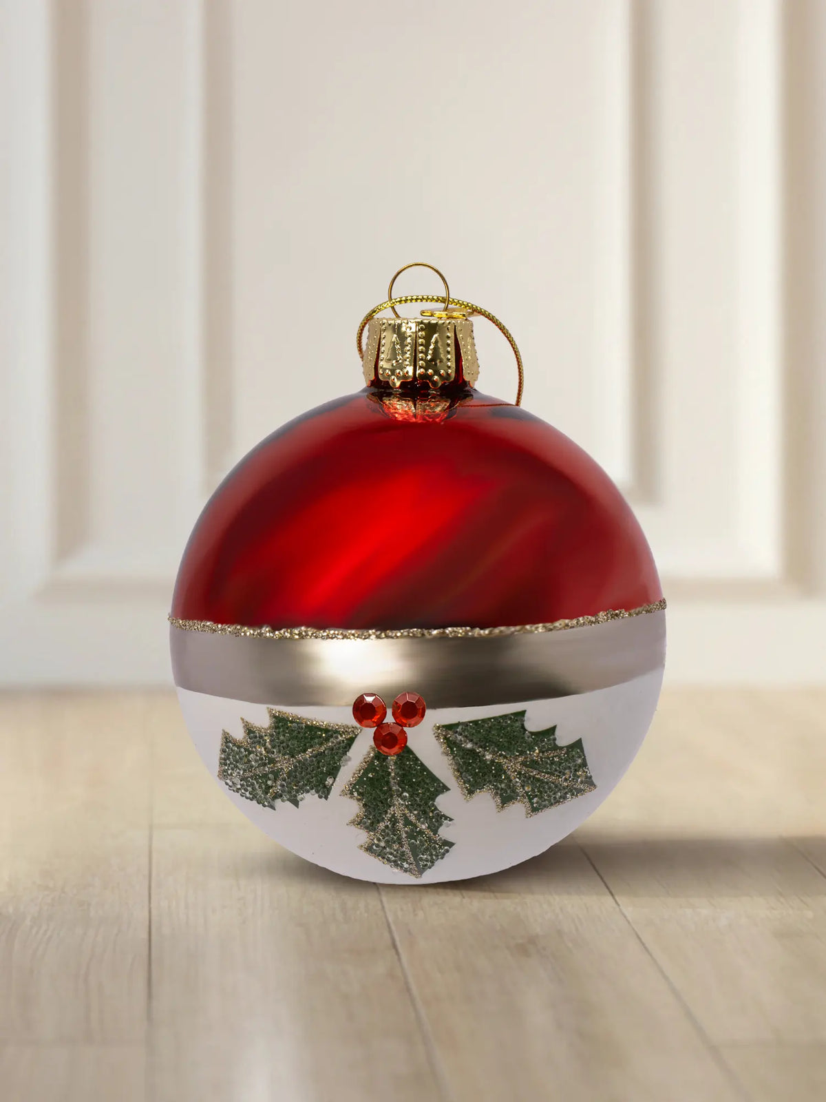 Glaskugel Winterbeerenzweig 8cm: obere Hälfte rot glänzend, untere Hälfte weiß matt, goldener Glitzerstreifen als Trennlinie, grüne Stechpalmenzweige mit roten Straßsteinen, goldener Aufhänger mit goldener Kordel