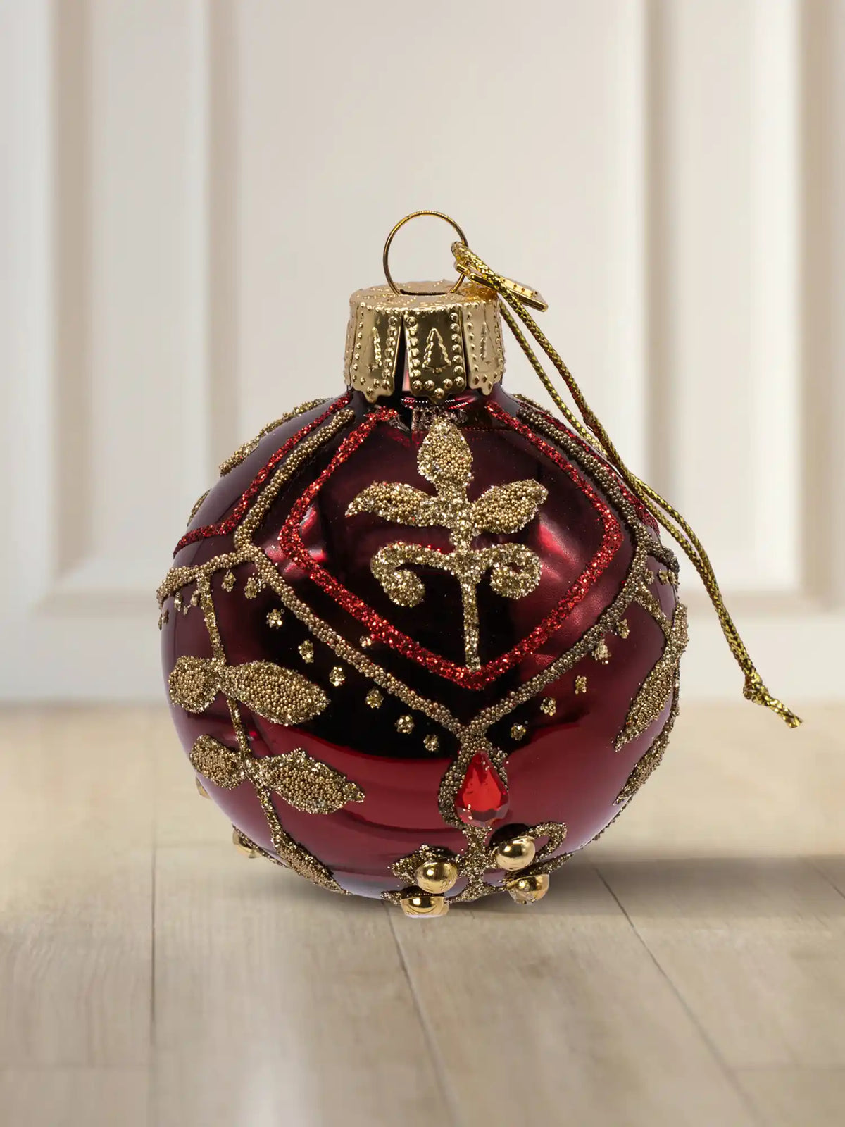 Glaskugel Bordeaux glanz 10cm: bordeauxrote Glaskugel mit Glanzfinish, aufwendiges goldenes Dekor aus Perlen und Straßsteinen, florales Muster mit rotem Glitter, goldener Aufhänger mit goldener Kordel