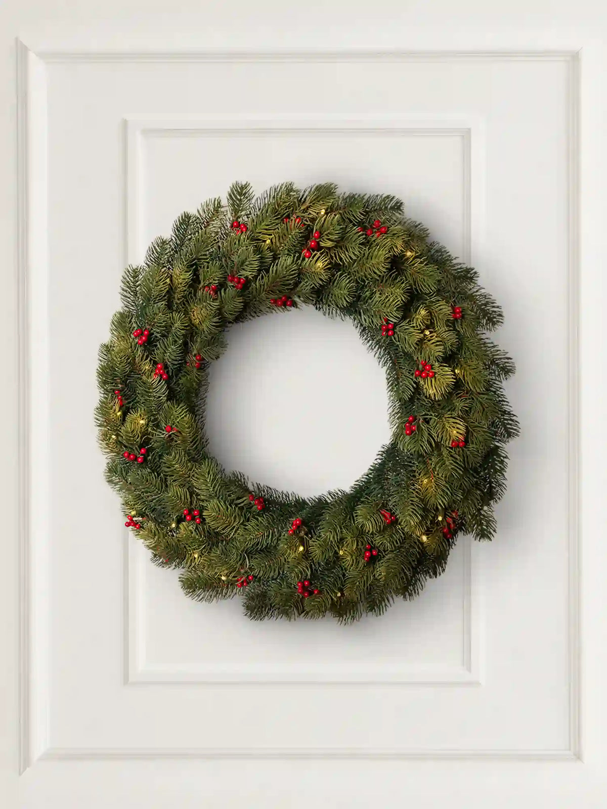 Ghirlanda natalizia ArtiTree con bacche rosse e luci LED, appesa come decorazione a una parete chiara in un accogliente soggiorno