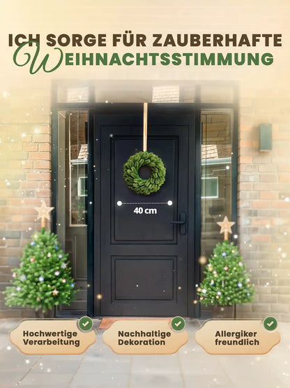Künstlicher 40 cm Weihnachtskranz an schwarzer Haustür zwischen zwei geschmückten Weihnachtsbäumen